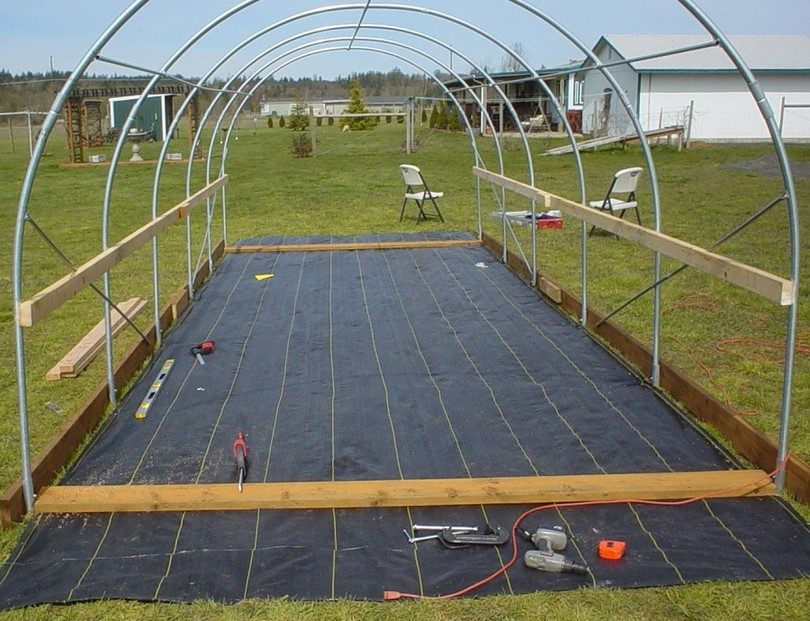 Incomplete greenhouse frame in a field. Tools on the ground.