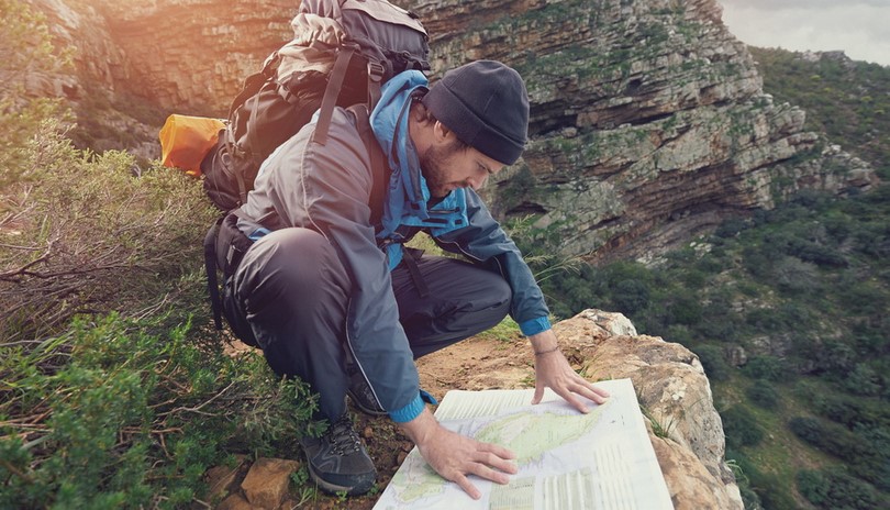 Lost hiker with backpack checks map to find directions in wilder